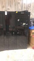 Front view of closed black Stack-On cabinet showing two doors with locks and keys attached