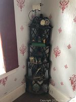 Full view of dark wood corner shelf placed in corner of room with wallpaper showing decorative items on multiple shelves.