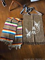 Serape blanket laid next to tan canvas apron showing rainbow stripes and printed Japanese characters