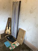 Photo of the acoustic guitar leaning against wall beside the boxed autoharp and folded room divider.