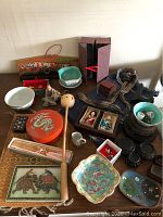 Overview of entire lot on tabletop including bowls, dishes, coasters, figurines, fan and decorative boxes