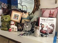 Image showing assortment of cat-themed decorative items including several cat figurines, cookie jars, a framed cat picture, and The New Yorker cat cartoons book.