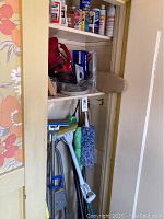 Open closet with shelves of cleaning products and hanging cleaning tools