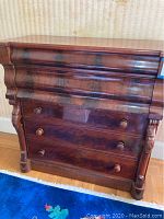 Front view showing five drawers with round knobs and marbled wood finish with subtle ornamental side carvings.