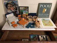 Overview of lot items on marble surface including framed needlepoint, Winnie the Pooh prints, doll furniture pieces