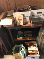 Wide shot of five boxes and one bag of assorted books on shelves and floor, showing various book sizes and colors
