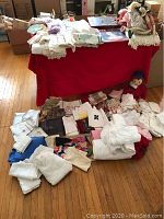 Overview of table covered in red cloth with assorted linens and dolls spread out