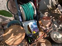 Photo showing garden hose on black metal wind-up reel besides various plant pots and bucket with river rocks.
