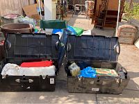 Two large black storage bins open displaying assorted camping gear including sleeping bags and boxed lantern