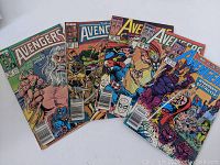 Five vintage Marvel Avengers comic books laid out fanned on a white background showing the colorful iconic covers of various issues.