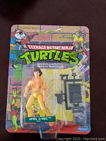 Front of original blister pack showing April O'Neil action figure in yellow and orange outfit with black accessories included. Brightly illustrated TMNT logo and characters on backing card.