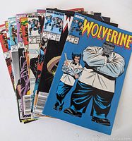 Photo showing a fanned set of nine Wolverine comic books with visible Marvel logos and various cover art of Wolverine and other characters including large figure in white jacket.