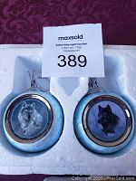 Two Bradford Exchange wolf ornaments in blue and silver, one with a grey wolf and one with a black wolf, in foam packaging.