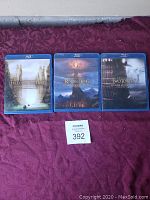 Photo of three Blu-ray cases from Lord of the Rings trilogy (Fellowship of the Ring, The Return of the King, The Two Towers) arranged side by side on a purple cloth background.