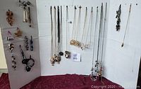 Photo of costume jewelry displayed on white boards with a burgundy cloth underneath, showing earrings on the left, necklaces in the center and right, bracelets on the left insert.