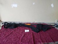 Truck cargo net laid on a maroon textured surface, showing the netting, elastic edges, and metal hooks for attachment.