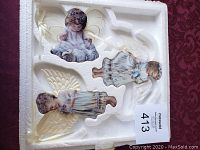 Three Bradford Exchange angel ornaments in white molded Styrofoam packaging on a red background.