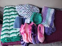 Handmade crocheted blanket, poncho, slippers, scarf, shawl, and bag all displayed together on a flat surface.