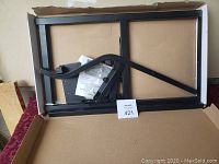 Top view of black metal frame tailgate ladder and mounting hardware in a cardboard box.