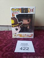 Funko Pop figure of Rick Grimes from The Walking Dead in original packaging with auction lot number on table.