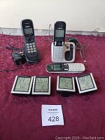 Four Acurite digital temperature gauges with black frames and LCD screens, along with three cordless phones including two Uniden models and one unknown brand, all placed on a red cloth surface.