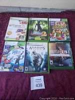 Six Xbox and Xbox 360 games laid out on a purple cloth, showing front covers and cases.