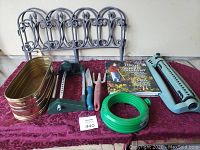 Photo showing the full lot with two blue plastic sprinklers, three hand gardening tools with blue/red handles, two metal decorative garden fences, one metal rectangular planter, a green garden hose connector, and a gardening book.