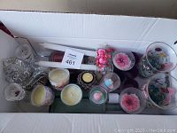Photo showing an assortment of crystal and glass candle holders, two hand-painted glass holders with floral designs, and various small and taper candles arranged in a white box.
