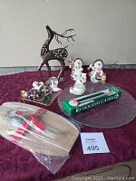 Photo showing all items on a red cloth including moose ornament with broken antler on glass, metal deer figurine, holiday candles in box, wooden serving tray with spreader, glass serving platter, and various Christmas figurines.