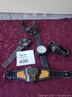 Photo showing five men's wristwatches on a purple textured cloth background with a MaxSold numbered card '498'.