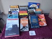 Photo showing an assortment of books from various authors including Stephen King, Dean Koontz, Michael Crichton, and J.R.R. Tolkien arranged on a purple tablecloth.