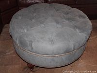 Side view of round button-tufted ottoman showing nailhead trim and wooden legs