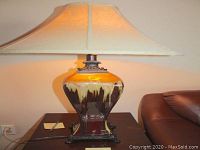 Full view of lamp showing glazed ceramic base in warm earth tones with decorative metal base and part of attached cord and switch on nearby table surface.
