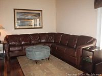 Full view of four piece brown leatherette sectional sofa in living room corner with carpet and round ottoman.
