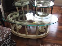 Angled view of the carved wood coffee table with glass top, showing swirl carved accents and oval base.