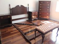 Full view of wooden full size bed parts disassembled on floor including headboard, footboard, side rails, two nightstands and cushioned bench.