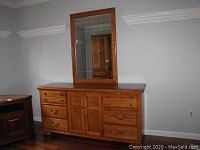 Front view of wooden dresser with attached rectangular mirror on top.