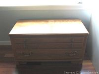 Front view of wooden chest showing faux three drawer fronts with brass tone handles and lift-up lid top.