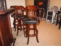 Three solid wood swivel bar stools with curved slat backs and black leatherette seats with nailhead trim, placed beside a wooden bar.
