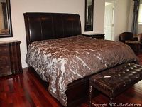 Main bedroom setup showing the bed dressed with bedding, showing the leather upholstered headboard and matching footboard and side rails, with a leather tufted bench at the foot.
