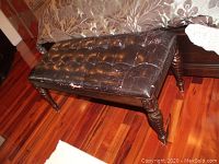 Full view of bench showing tufted, heavily cracked bonded leather top and wooden base.