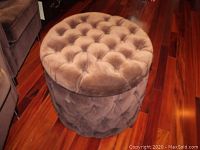 Angle showing round velvet button tufted ottoman on wood floor