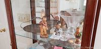 Image showing two wide-mouthed clear glass bowls, small glass cup, and Hummel figurines on a glass shelf.