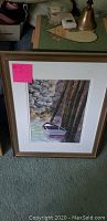 Framed watercolor painting showing a boat alongside pilings and rocks with a pink note attached.