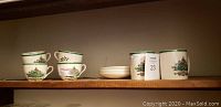 View of 2 Spode Christmas mugs, 4 cups, and 4 saucers set on a wooden shelf.