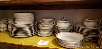 Noritake Hanover vintage bone china stacked on two shelves showing plates, bowls, cups, and saucers with gold trim and floral decorations.