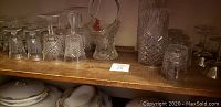 Top shelf wooden display with assorted glasses including diamond-patterned tumblers, stemmed glasses, and a glass basket bowl.