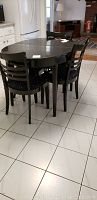 Full view of black oval dining table with four matching chairs, showing one chair missing partial backrest