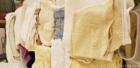 Close-up showing various linens, towels, and napkins folded and stacked in a container, neutral colors seen