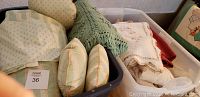 Two bags containing assorted linens including comforters, pillows, throws, and other fabric items arranged in bins.